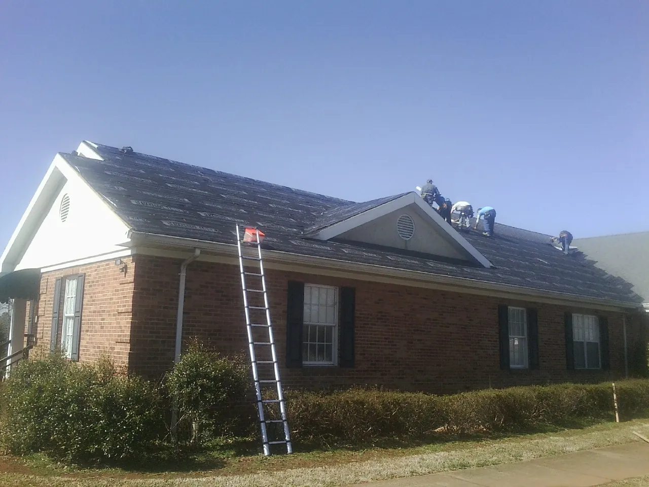 Crew tearing shingles off a brick ranch roof with a ladder set — Metal Roof Repair work by our crew in Red Hook