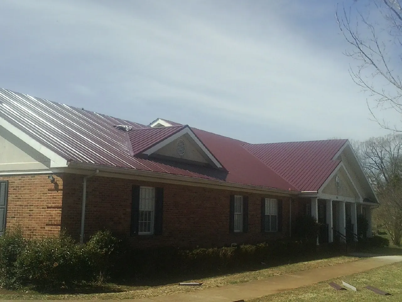 Red metal roof with gabled entries on a long brick building, from a Hail Damage Roof Repair job in Red Hook