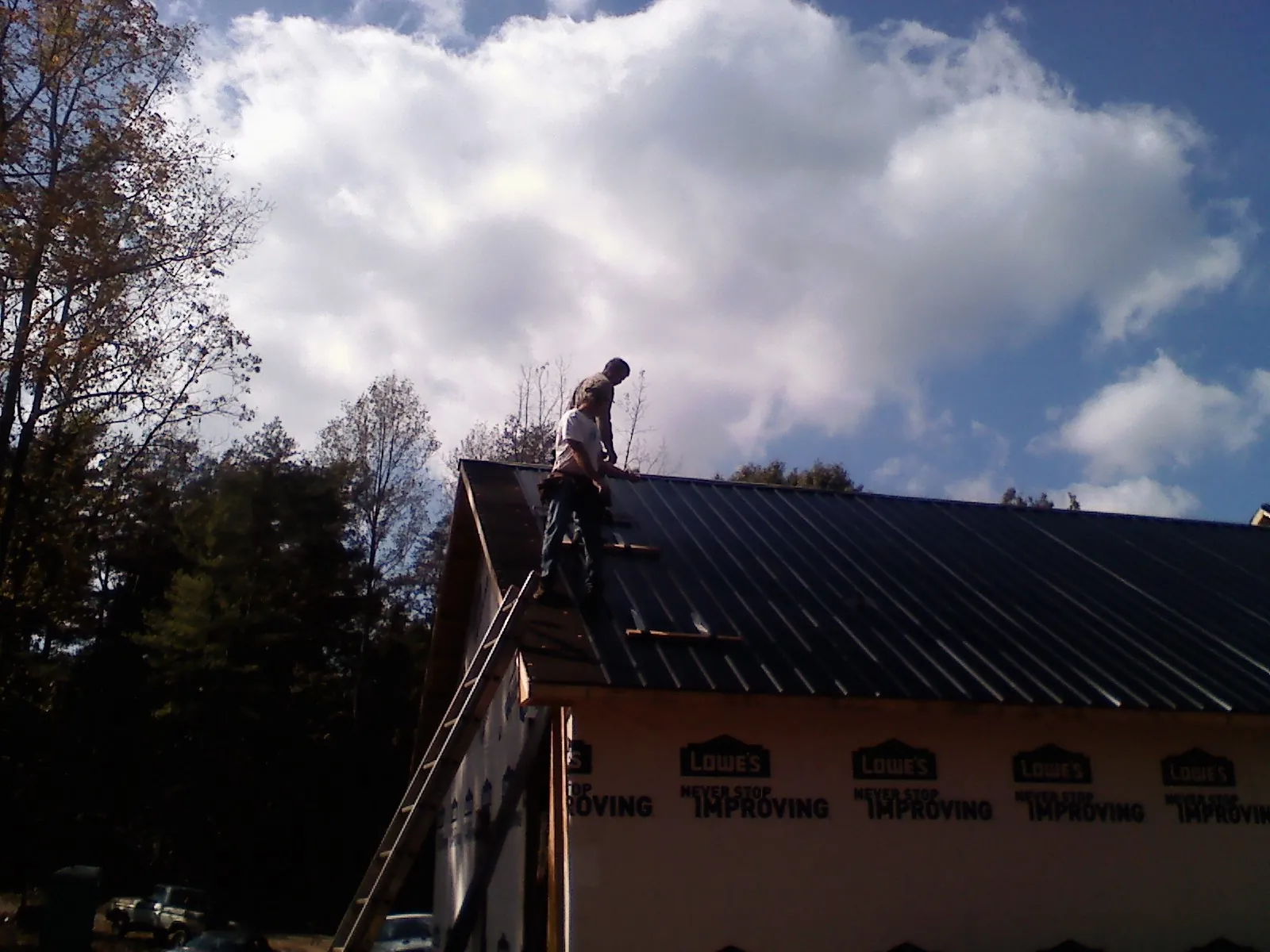 Roofer fastening dark metal panels high against a cloudy sky, from a Roof Inspection job in Red Hook