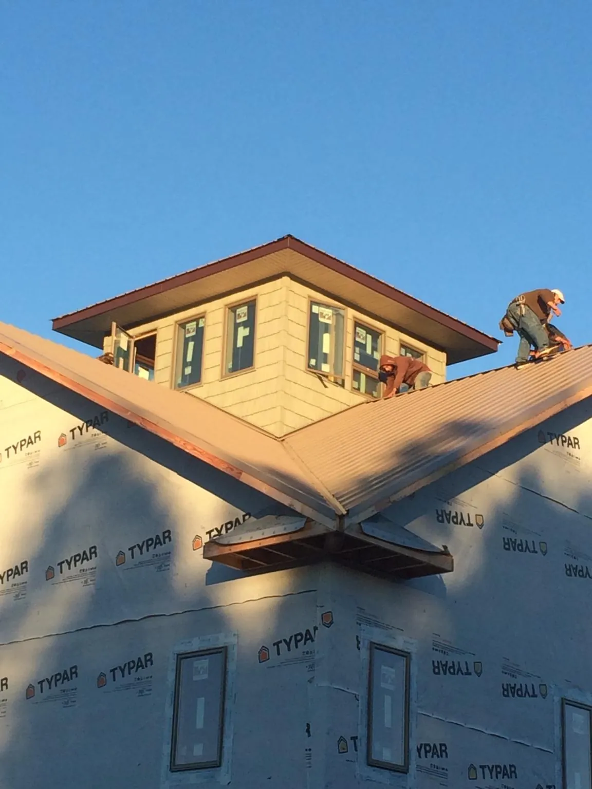 Roofers working around a rooftop cupola on a new metal roof at sunset — Roof Waterproofing in Red Hook by Roofing Brothers